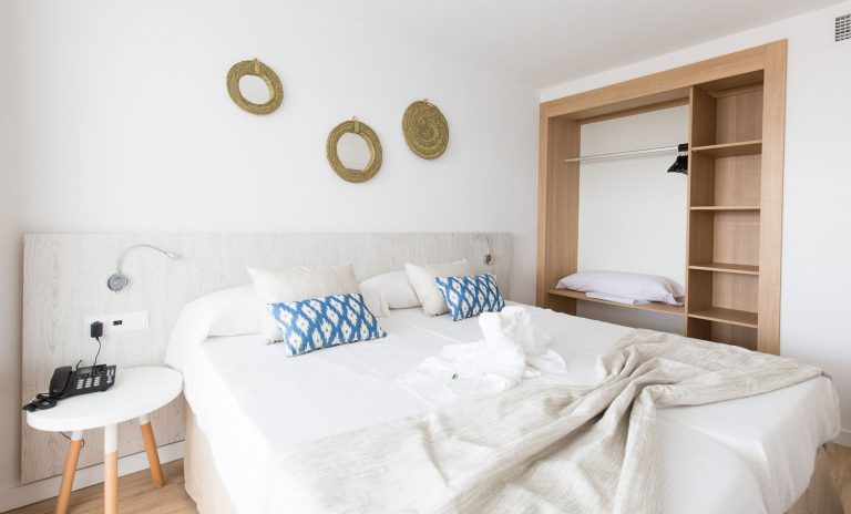 Habitación con ropa de cama blanca y cojines de tela de llengües típica mallorquina en Apartamentos Ses Roquetes.
