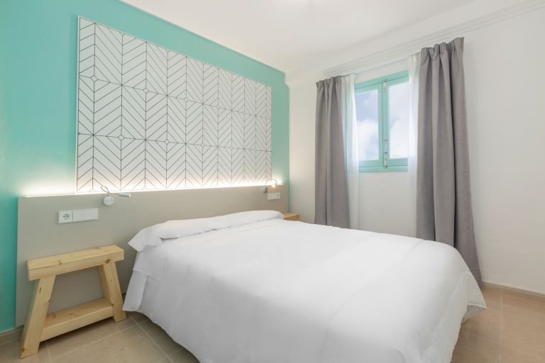 Dormitorio doble en habitación de apartamentos Los Arcos, con pared en contraste en tono aguamarina.