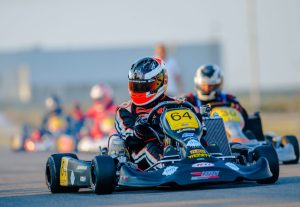 Piloto, vestido con casco y mono, conduciendo un kart en un circuito.