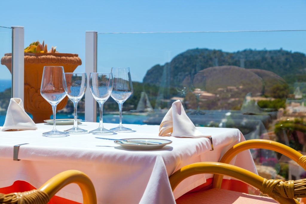 Mesa de restaurante con un mantel blanco y copas de vino vacías con vistas al mar.