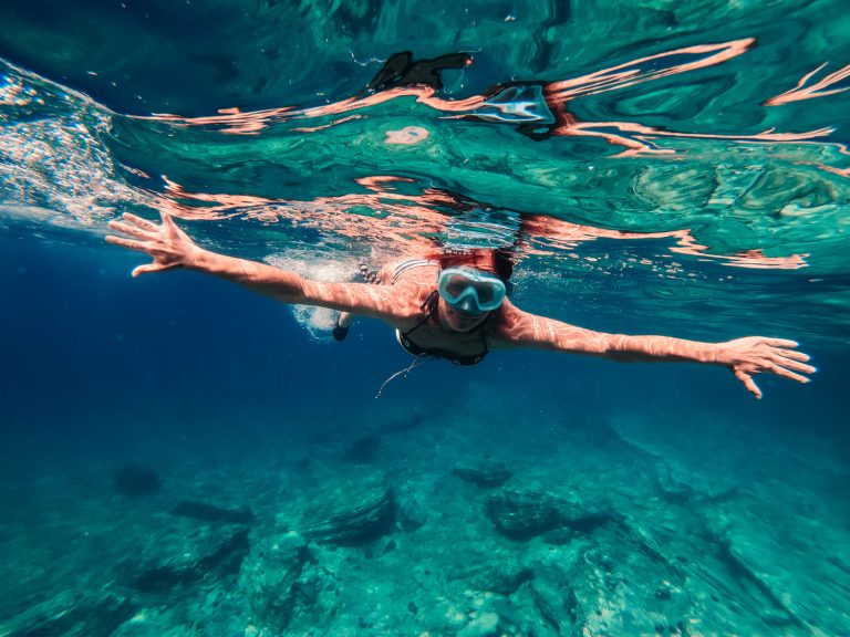 Chica nadando con gafas de buceo, sumergida en el mar.